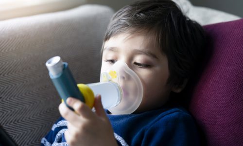 Close up kid face using volumtic for breathing treatment,Poor boy have a problem with chest coughing holding inhaler mask,  Child having asthma allergy using the asthma inhaler, Healthcare concept